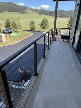 Black cable railing along a covered balcony overlooking green hills