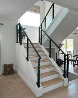 Black posts and top rails with cable infill on knee walls along a white stair with light oak treads.