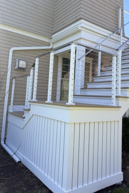 White cable railing posts line a staircase rising along a shingled house to an upper deck