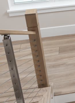 Close detail of a stainless cable post meeting a square wood newel with wood handrail.