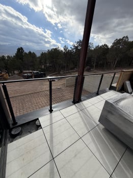 Black cable railing on a tiled deck above a wooded hillside