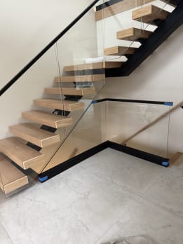 Floating white oak stair with frameless glass in a black base rail wrapping the stair base