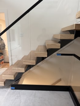 Side view of white oak floating treads beside frameless glass and a black base rail