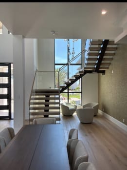 FLIGHT Mono floating stair with glass railing rising past a window wall beyond a dining table