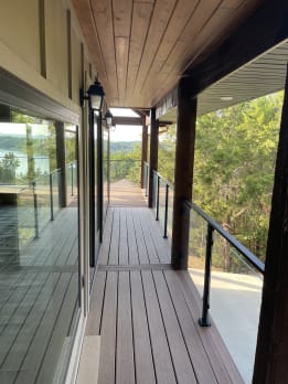 Long covered deck walkway lined with black-post glass railing and timber posts