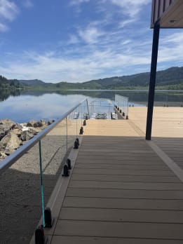 Frameless glass on dark talon spigots lines a composite deck reaching out over a calm mountain lake