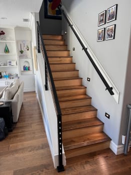 Looking up a stained wood stair with a black wall-mounted handrail and black cable railing.