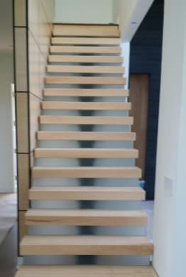 Thick maple treads cantilevered from a paneled wall seen straight up the flight.