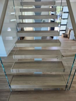 Head-on view of thick white oak floating treads between two frameless glass railings