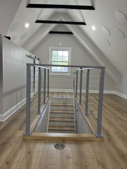 Silver cable railing guards a stair opening in a bright attic bonus room with wood floors.