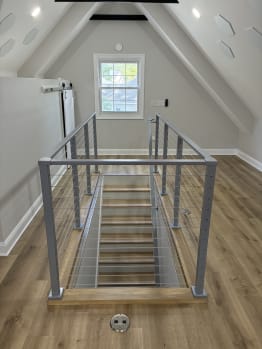 Symmetric view of a stair opening framed by silver cable railing in a vaulted attic room.