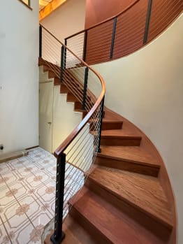 Black posts and stainless horizontal infill follow a curved Brazilian cherry staircase with a wood handrail.