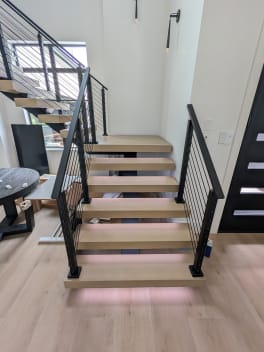 White oak floating treads with LED underglow and black cable railing on both sides in a modern stairwell.