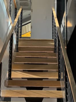 Wood treads on a black mono stringer climb between cable railings with wood handrails toward a bright landing.