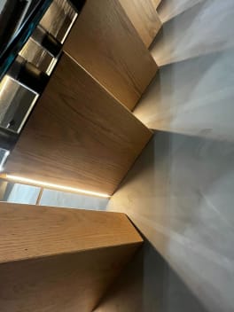 Underside view of white oak cantilever treads with LED strips casting light across a plaster wall.