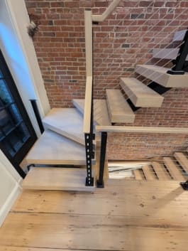 Pale oak floating treads turning at a landing with black cable railing against a brick wall
