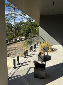 Frameless glass on black talon spigots lines a concrete terrace among coastal pines