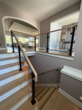 Black posts with clear laminated glass panels and white oak handrail wrap a bright stairwell opening.