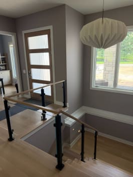 Black-post glass railing with white oak handrail guards a stair opening near a front door.