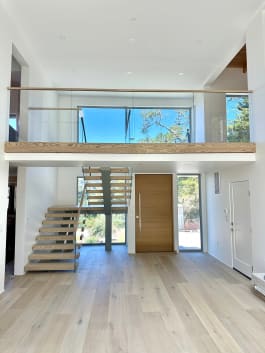Bright modern interior with a frameless glass loft railing above a wood fascia and floating wood stair with glass guard below.