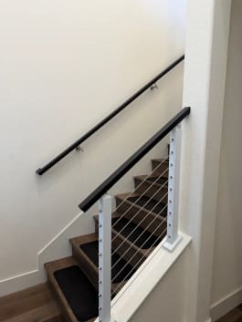 Bright white cable posts with a black top rail and matching wall handrail along an interior stair.