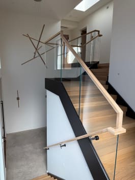 Frameless glass with a light wood handrail and a wall-mounted handrail line a wide oak stair under a sculptural light.