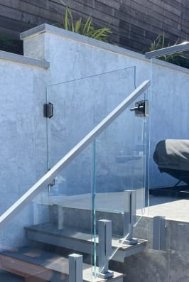 Clear glass panels on talon clamps with a stainless handrail follow an exterior stone stair by a pool deck.