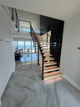Floating maple stair with LED treads and black cable railing in a marble-floored beach house