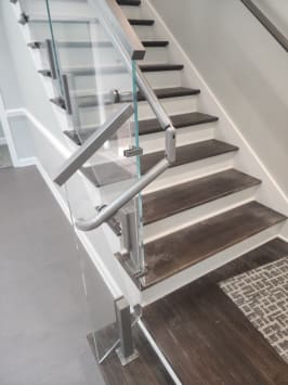 Stainless post glass railing with a looped stainless handrail return at a stair base