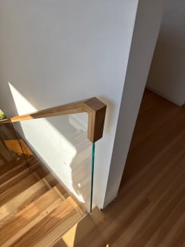 Ash handrail cap on frameless glass returning cleanly into a white wall above a stair