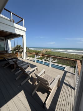 Cable railing with white posts and wood cap rail lines a beach house deck above a pool and ocean.