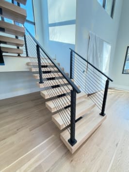 Close view of white oak floating treads on a black mono stringer with black cable railing at the stair base.