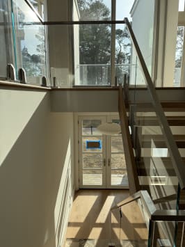 Frameless glass panels in stainless clamps with a square stainless handrail along an open oak stair facing tall windows.