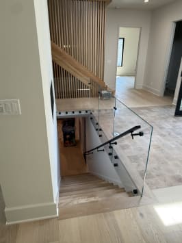 Glass panels on black standoff pins with a black handrail guard a stair opening beside a slatted wood wall.