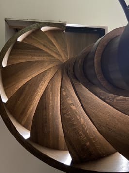 Looking up into a wood-wrapped spiral stair with fanned oak treads and glowing LED tread lights.