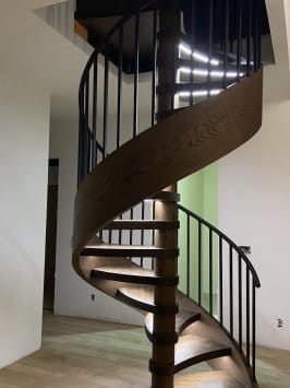 A custom spiral stair with a curved dark oak stringer, black balusters and LED-lit treads.