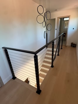 A black cable railing wraps an oak stairwell beneath a sculptural ring chandelier.