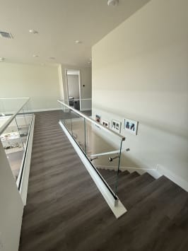 Frameless glass in a white base shoe with a slim cap and a glass-mounted handrail follows a dark-plank stair down from an upper hall.