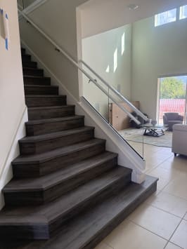 A dark-plank stair rises between a white wall handrail and a frameless glass guard with a glass-mounted handrail.