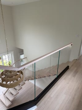 Looking down past a base-rail glass guard with oak handrail onto white-oak floating treads and a woven pendant.