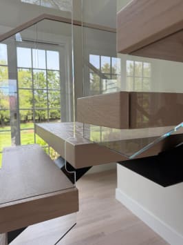 Close detail of thick white-oak floating treads and frameless glass panels against windows.