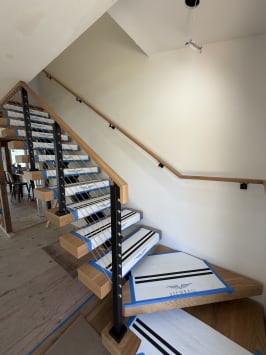 Viewrail-covered floating treads wind up beside a black-post cable railing and a wall-mounted oak handrail.