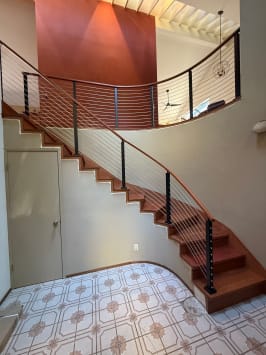 Curved stair and balcony with black posts and cable infill in a two-story foyer.