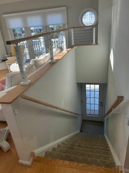 White posts and cable railing with wood cap rail guard a stair opening in a coastal-style home.