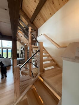 Open wood stair with square wood newels, wood handrails and cable infill in a timber-beamed great room.