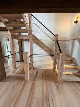 Rustic timber stair with chunky wood newels and black cable railing climbing to a landing.