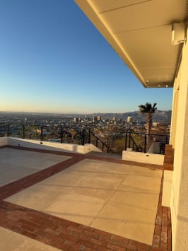 Black cable railing edges a paver-and-brick rooftop terrace overlooking a city and mountains at sunset.