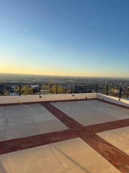 Cable railing tops a low wall around a brick-banded rooftop terrace with a sunset city view.