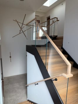 Frameless glass with a light wood handrail and a wall-mounted handrail line a wide oak stair under a sculptural light.