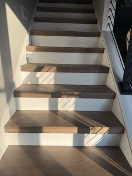 Dark oak thick-nose treads over white risers rise beside a black railing in afternoon light.